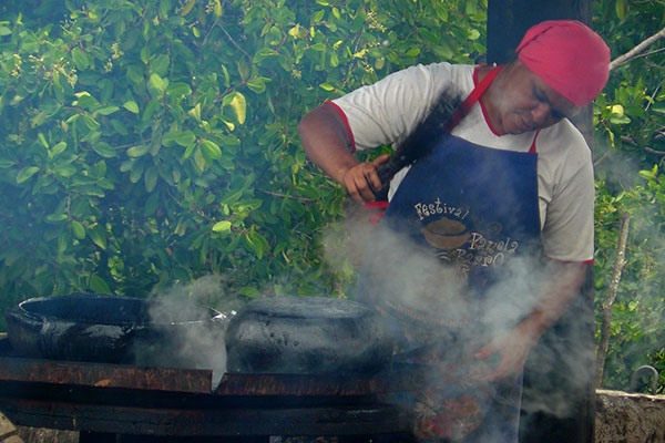 Artesã pintando a panela de barro de preto com a tintura extraida da casca da árvore do mangue